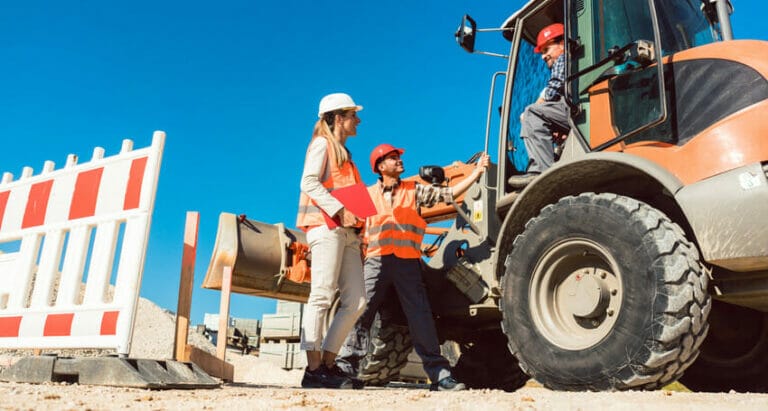 Two construction workers standing next to a bulldozer.