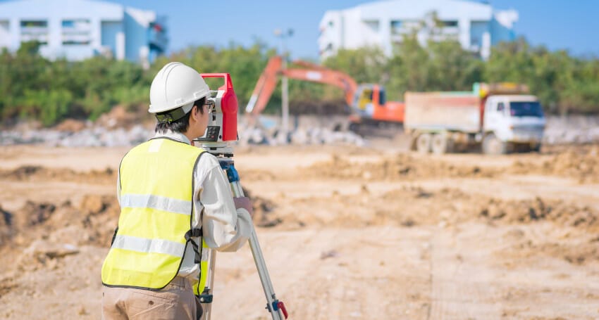 A construction worker looking at a surveyor's equipment.