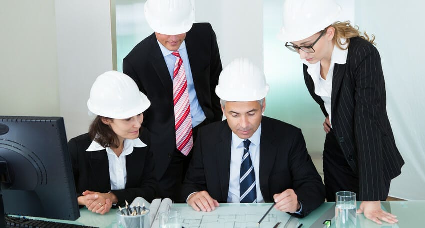 A group of civil engineers in hard hats examining plans.